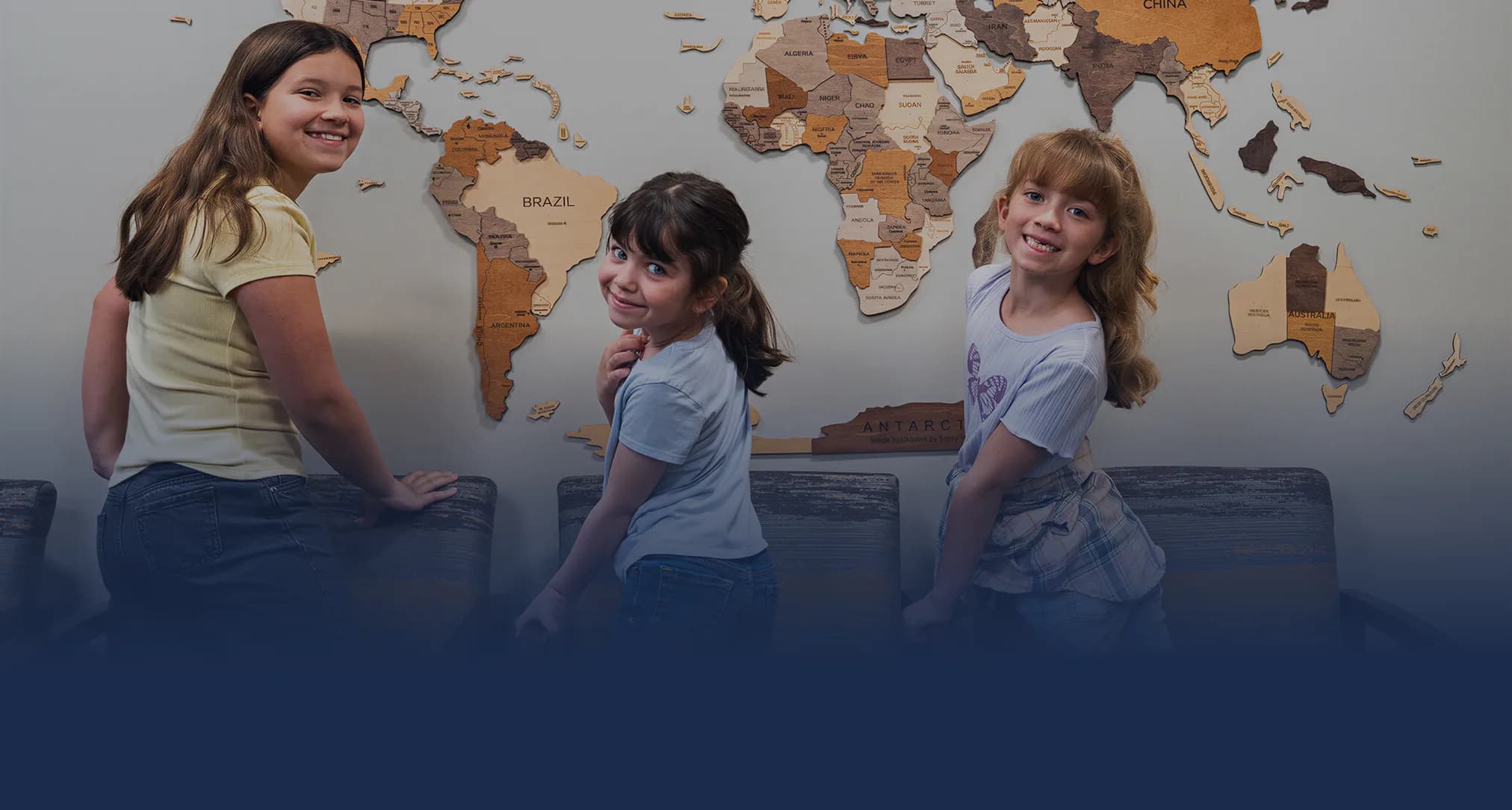 Three smiling kids in front of the world map in the Atlas Dental waiting room