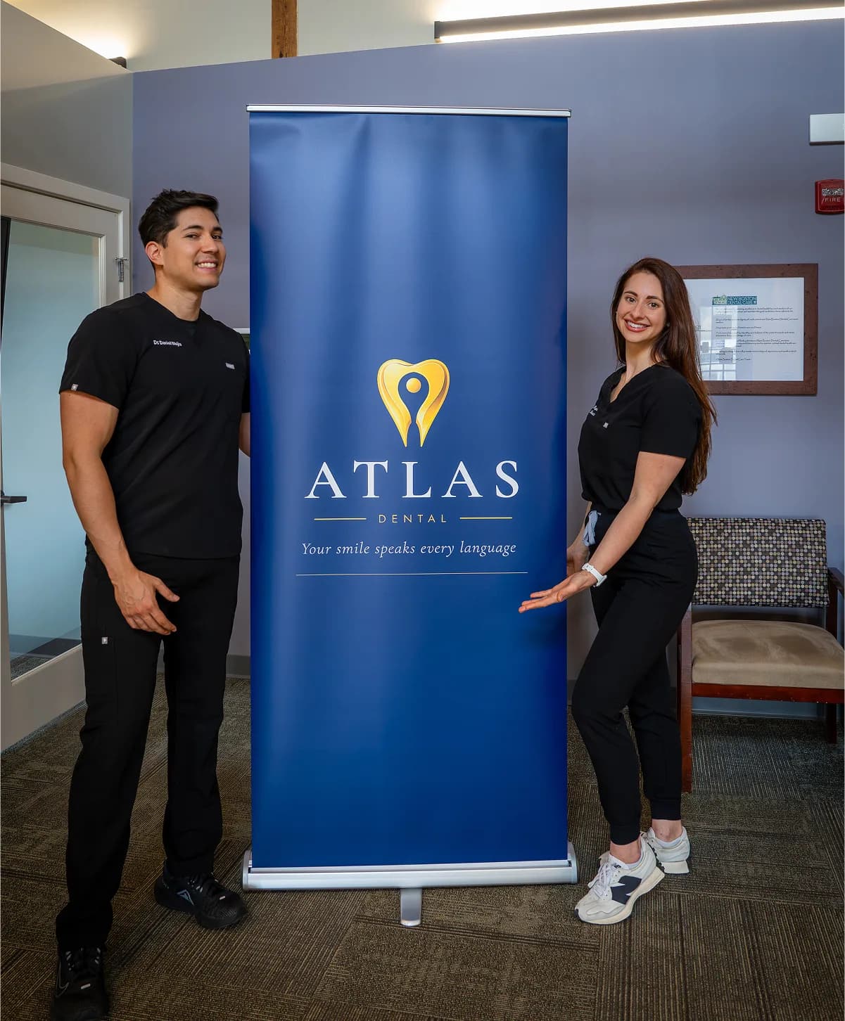 A professional photo of the owners standing beside a blue “ATLAS Dental” banner inside a modern dental office.